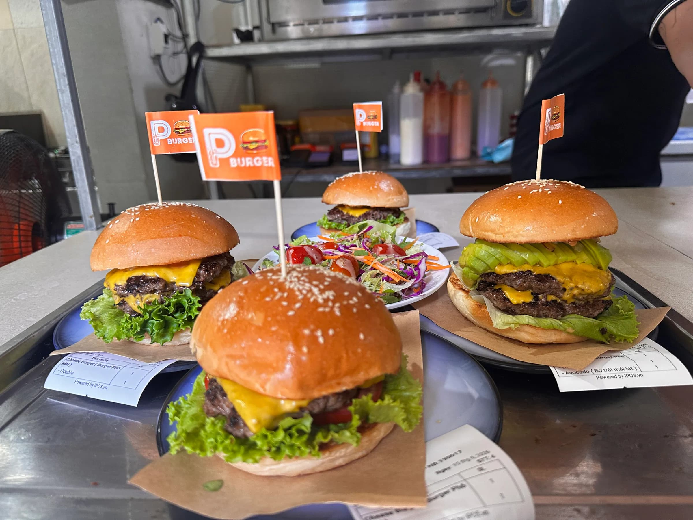 Three fresh burgers with P flags on the kitchen pass